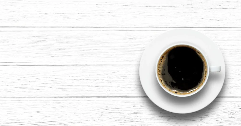 cup of black coffee on a white wooden table from above