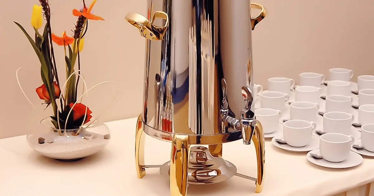 coffee urn on a table with cups and a flower vase