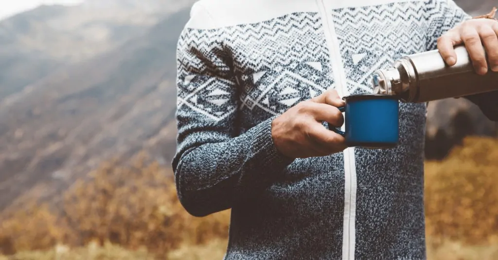 person pouring coffee into a mug in nature