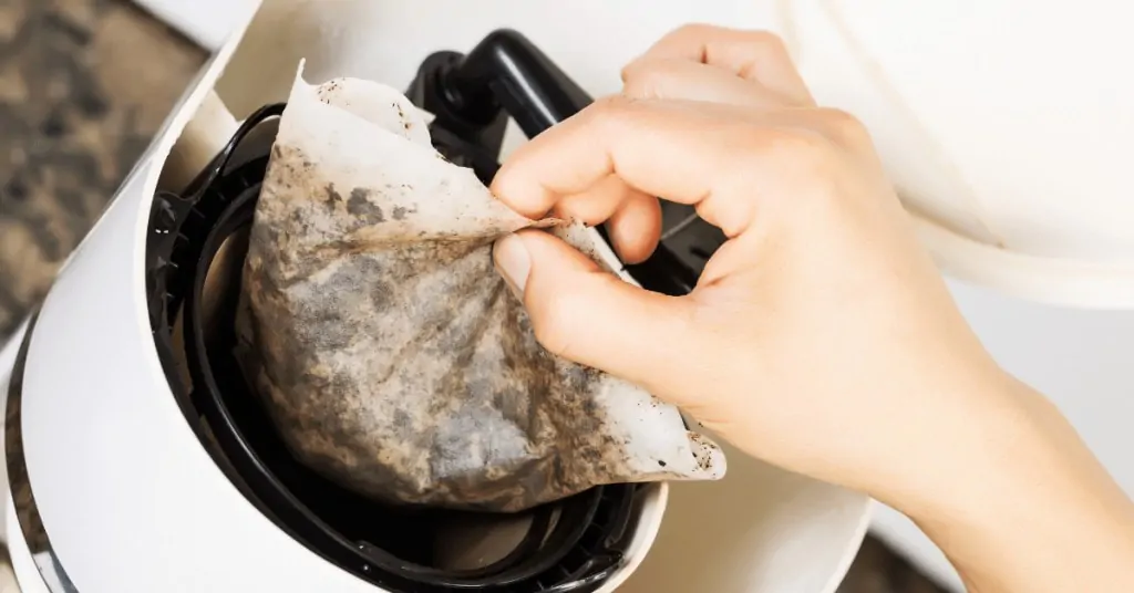 person taking a used coffee filter out of a coffee maker